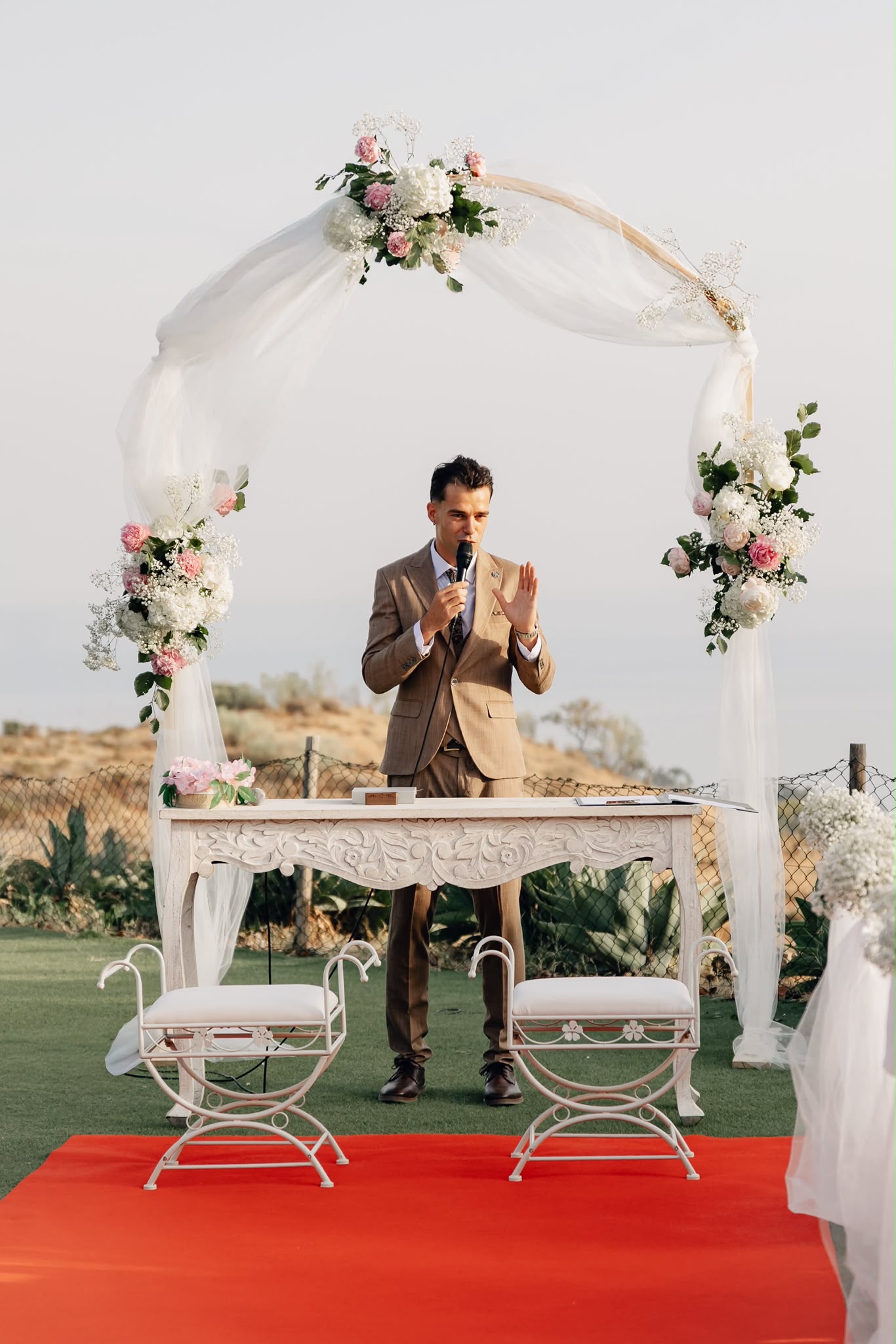 Vova leading an outdoor wedding ceremony beneath a floral arch